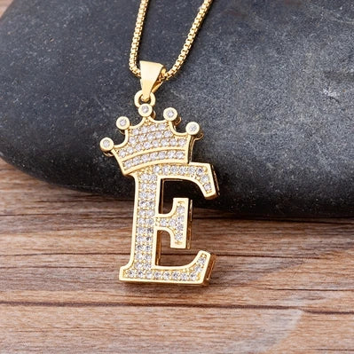 Gold necklace with a letter 'E' pendant on a stone and wood surface