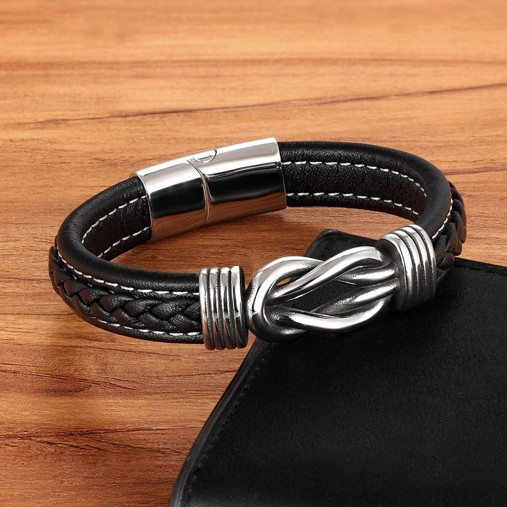Black braided leather bracelet with silver knot design and clasp on a wooden surface