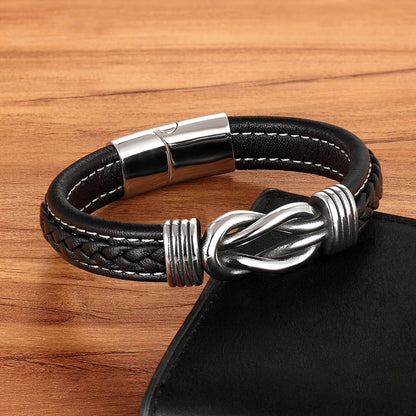 Black braided leather bracelet with silver knot design and clasp on a wooden surface