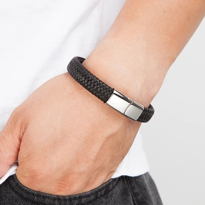 Person wearing a black braided bracelet with a silver clasp on a plain background