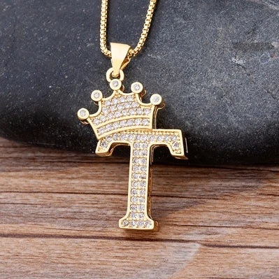 Gold letter 'T' pendant with crown design on a dark stone and wooden surface