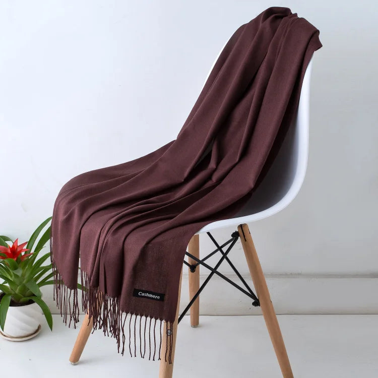 Brown throw blanket draped over a white chair with a plant in the background