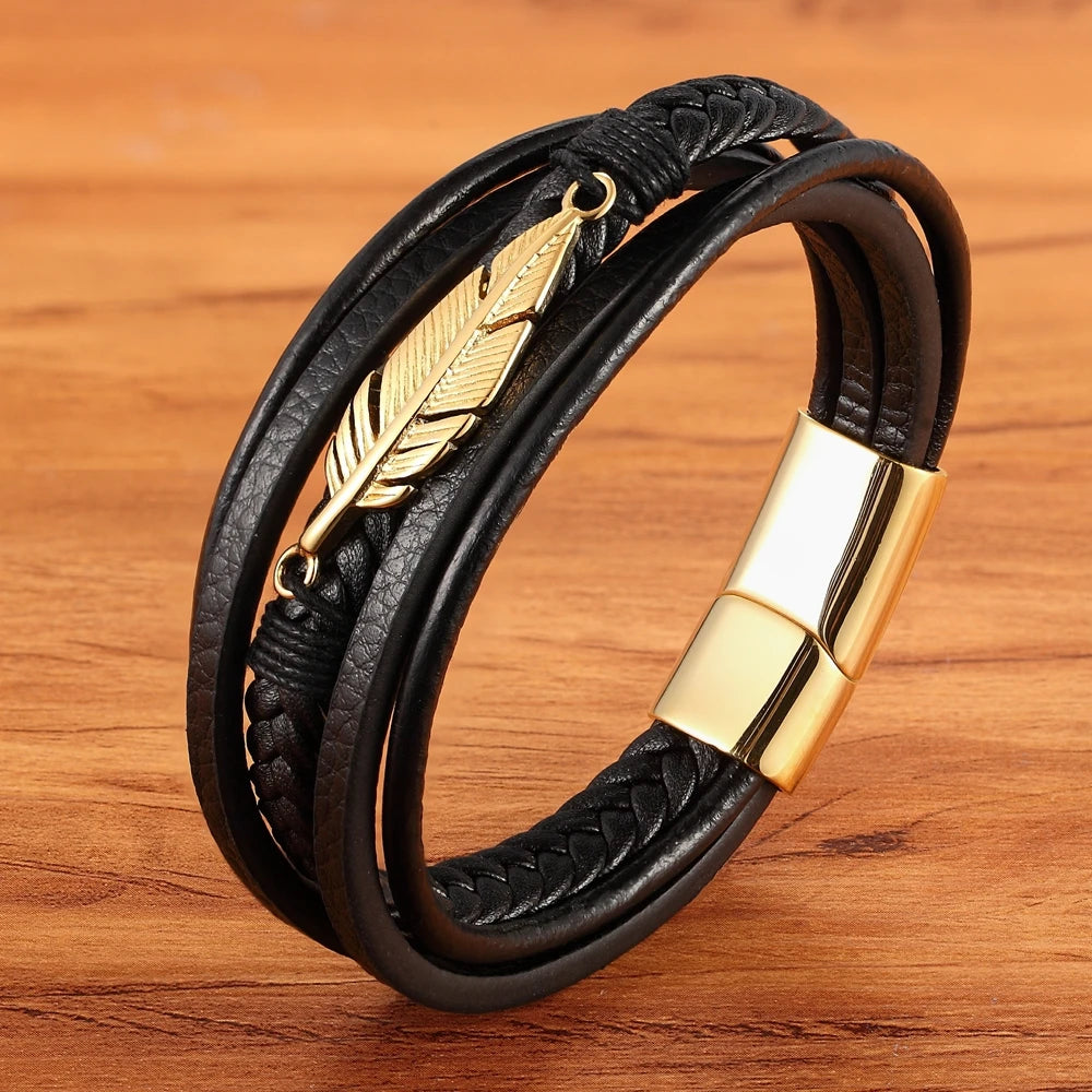 Black leather bracelet with gold feather charm and clasp on a wooden surface