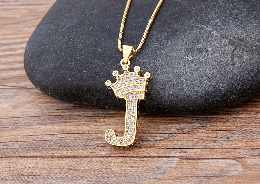 Gold letter 'J' pendant with a crown on a wooden surface