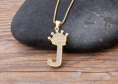 Gold letter 'J' pendant with a crown on a wooden surface