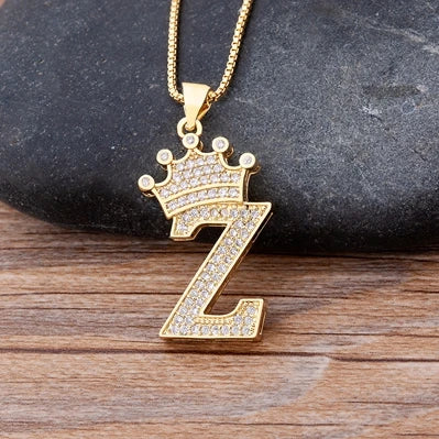 Gold necklace with a letter 'Z' pendant featuring a crown on a wooden surface.