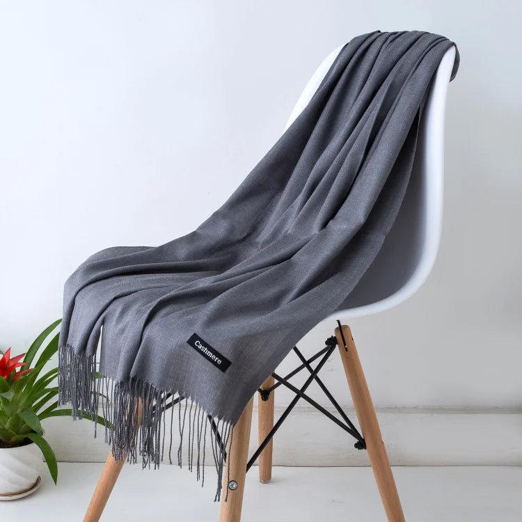 Grey scarf with fringes draped over a white chair against a light background