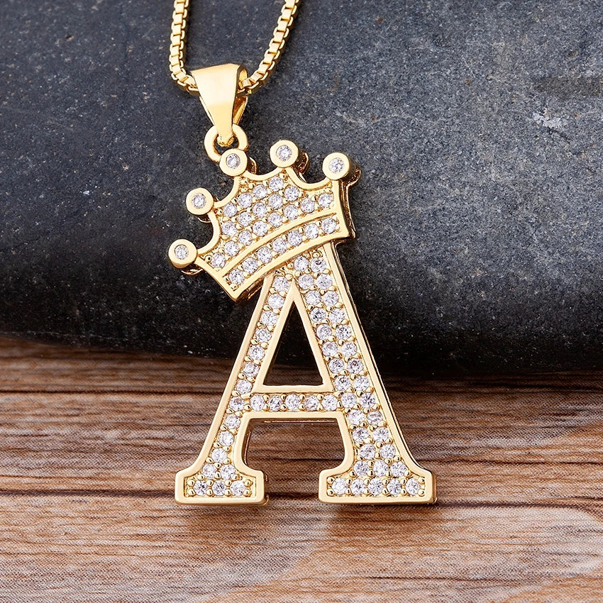 Gold necklace with a letter 'A' pendant featuring a crown design on a wooden surface.
