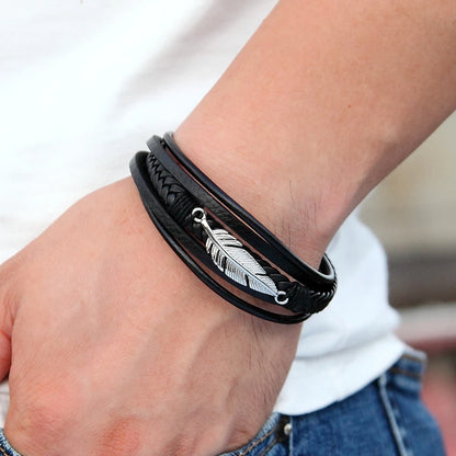 Black leather bracelet with feather charm on wrist against a blurred background