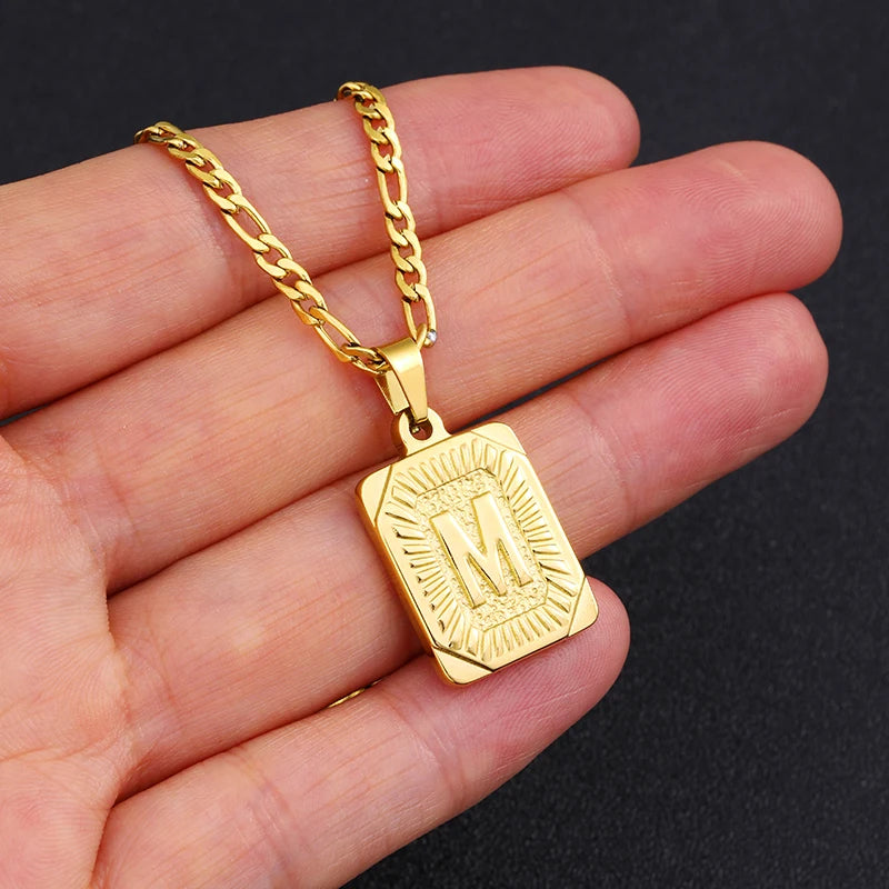 Gold necklace with a rectangular pendant on a hand against a black background