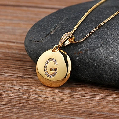 Gold necklace with a round pendant on a stone surface