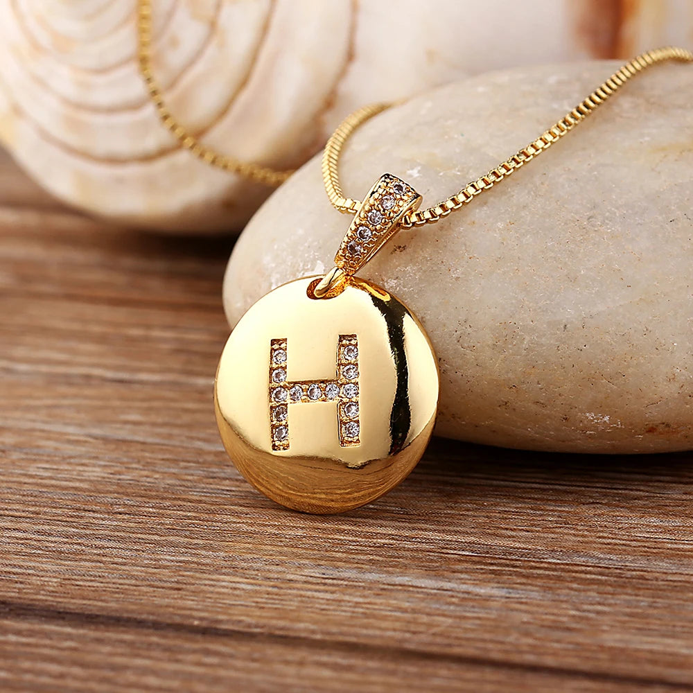 Gold necklace with a pendant featuring the letter 'H' on a wooden surface.
