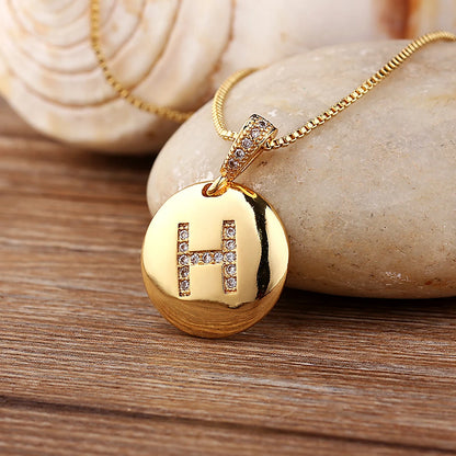 Gold necklace with a pendant featuring the letter 'H' on a wooden surface.