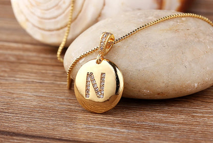 Gold necklace with a pendant featuring the letter 'N' on a wooden surface.