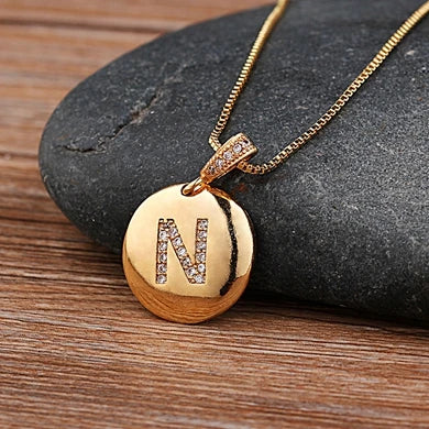 Gold necklace with a pendant featuring the letter 'N' on a stone surface