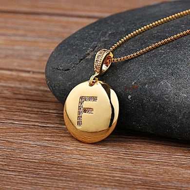 Gold necklace with a pendant featuring the letter 'F' on a stone surface