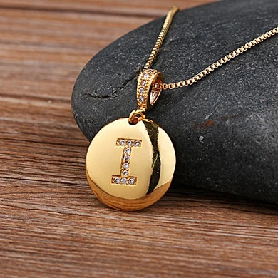 Gold necklace with a pendant featuring the letter 'I' on a stone surface