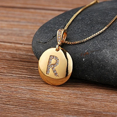 Gold necklace with a pendant featuring the letter 'R' on a stone surface