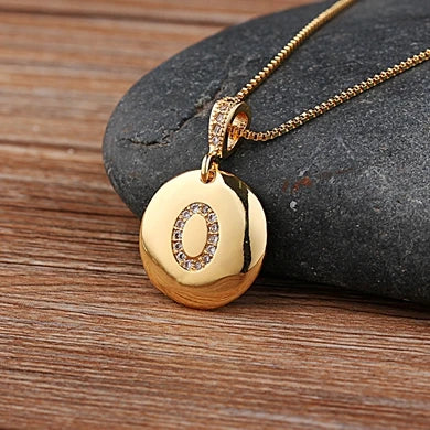 Gold necklace with a pendant featuring the letter 'O' on a wooden surface.