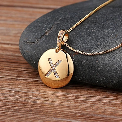 Gold necklace with a pendant featuring the letter 'X' on a stone surface