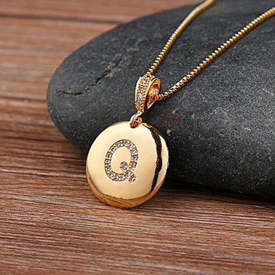 Gold necklace with a pendant featuring the letter 'Q' on a stone surface