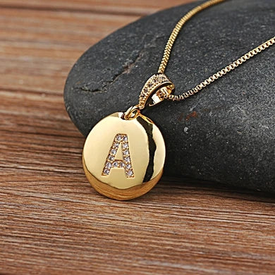 Gold necklace with a pendant featuring the letter 'A' on a stone surface