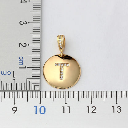 Gold pendant with letter 'T' next to a ruler for scale on a white background