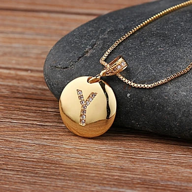 Gold necklace with a round pendant featuring the letter 'Y' on a stone surface.