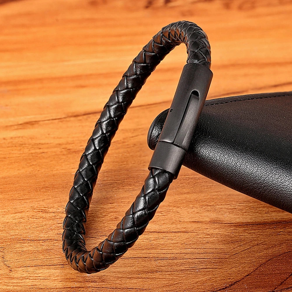 Black single strand braided leather bracelet with metal clasp on a wooden surface