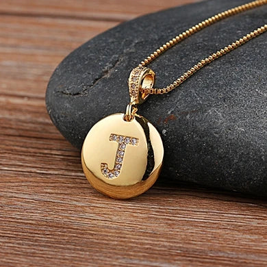 Gold necklace with a pendant featuring the letter 'J' on a stone surface.