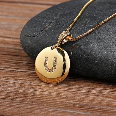 Gold necklace with a pendant featuring the letter 'U' on a stone surface