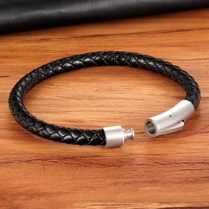 Black braided leather bracelet with silver clasp on a wooden surface