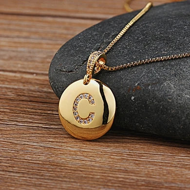 Gold necklace with a pendant featuring the letter 'C' on a stone surface