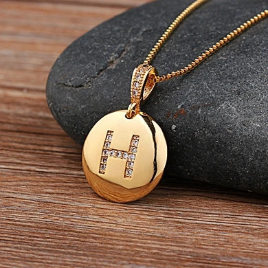 Gold necklace with a pendant featuring the letter 'H' on a stone surface