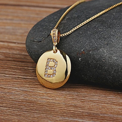 Gold necklace with a pendant featuring the letter 'B' on a stone surface