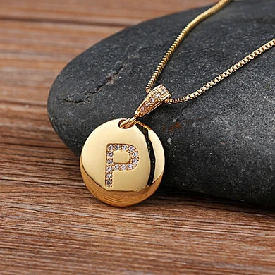 Gold necklace with a pendant featuring the letter 'P' on a stone surface