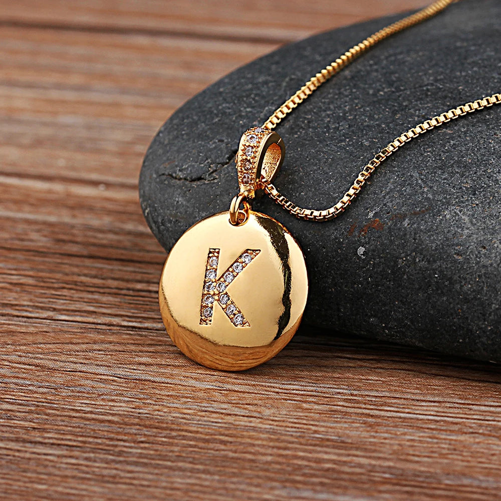Gold necklace with a pendant featuring the letter 'K' on a stone surface
