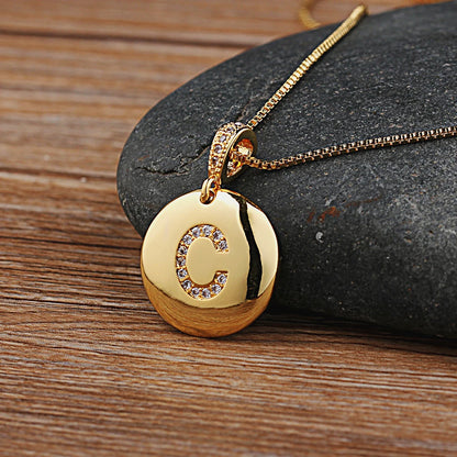 Gold necklace with a pendant featuring the letter 'C' on a stone surface