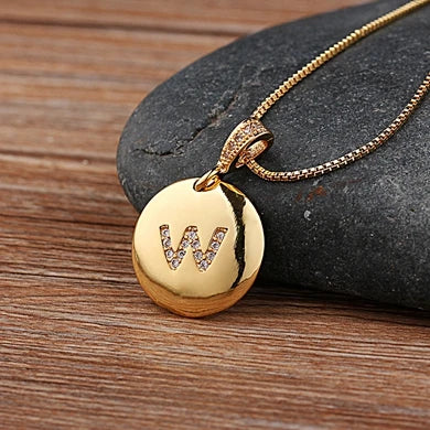 Gold necklace with a round pendant featuring the letter 'W' on a wooden surface.