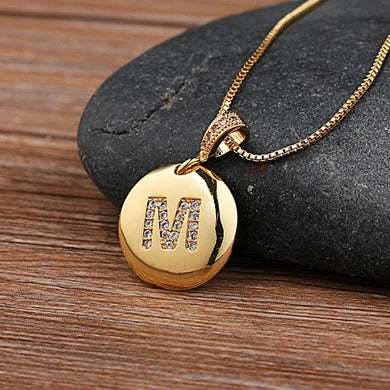 Gold necklace with a pendant featuring the letter 'M' on a stone surface