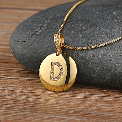 Gold necklace with a pendant featuring the letter 'D' on a stone surface