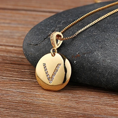 Gold necklace with a pendant featuring the letter 'V' on a stone surface