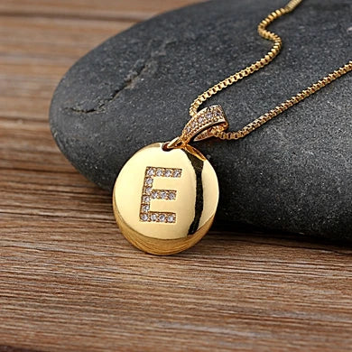Gold necklace with a pendant featuring the letter 'E' on a stone surface