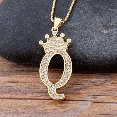 Gold necklace with a pendant shaped like the letter 'Q' on a dark stone and wooden surface.