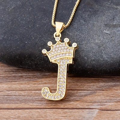 Gold letter 'J' pendant with crown design on a dark stone and wooden surface