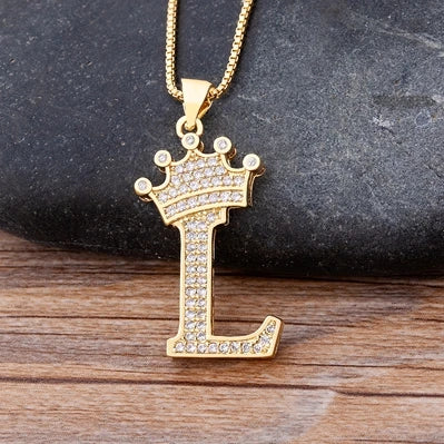Gold necklace with a letter 'L' pendant on a dark stone and wooden surface