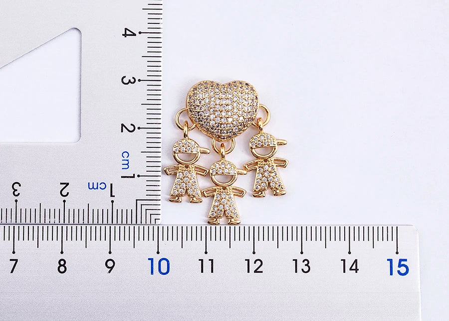 Gold charm with children and a heart shape next to a ruler for scale on a white background