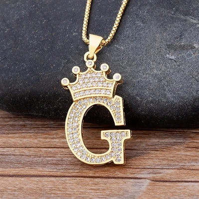 Gold necklace with a letter 'G' pendant on a dark stone and wooden surface