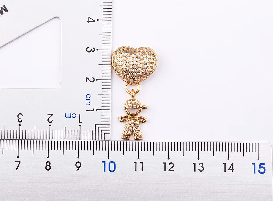 Gold heart-shaped charm with a child figure on a white background with a ruler for scale.