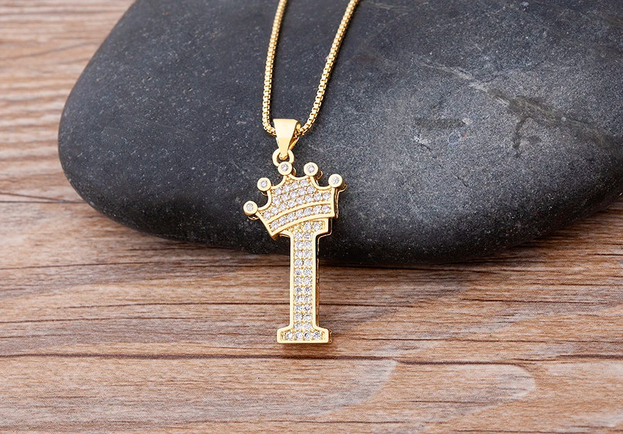 Gold necklace with a crown pendant on a stone surface